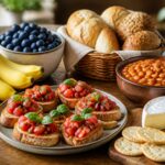 Mesa de madeira com diversas comidas que começam com a letra B, incluindo bananas, mirtilos, bruschetta, pães, feijão assado e queijo brie.